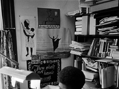 Writer Audre Lorde is photographed at a desk, surrounded by books and papers.