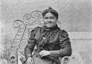 Mrs. Elizabeth Cisco is a Black woman seated in an ornate chair and wearing a formal full-length dress