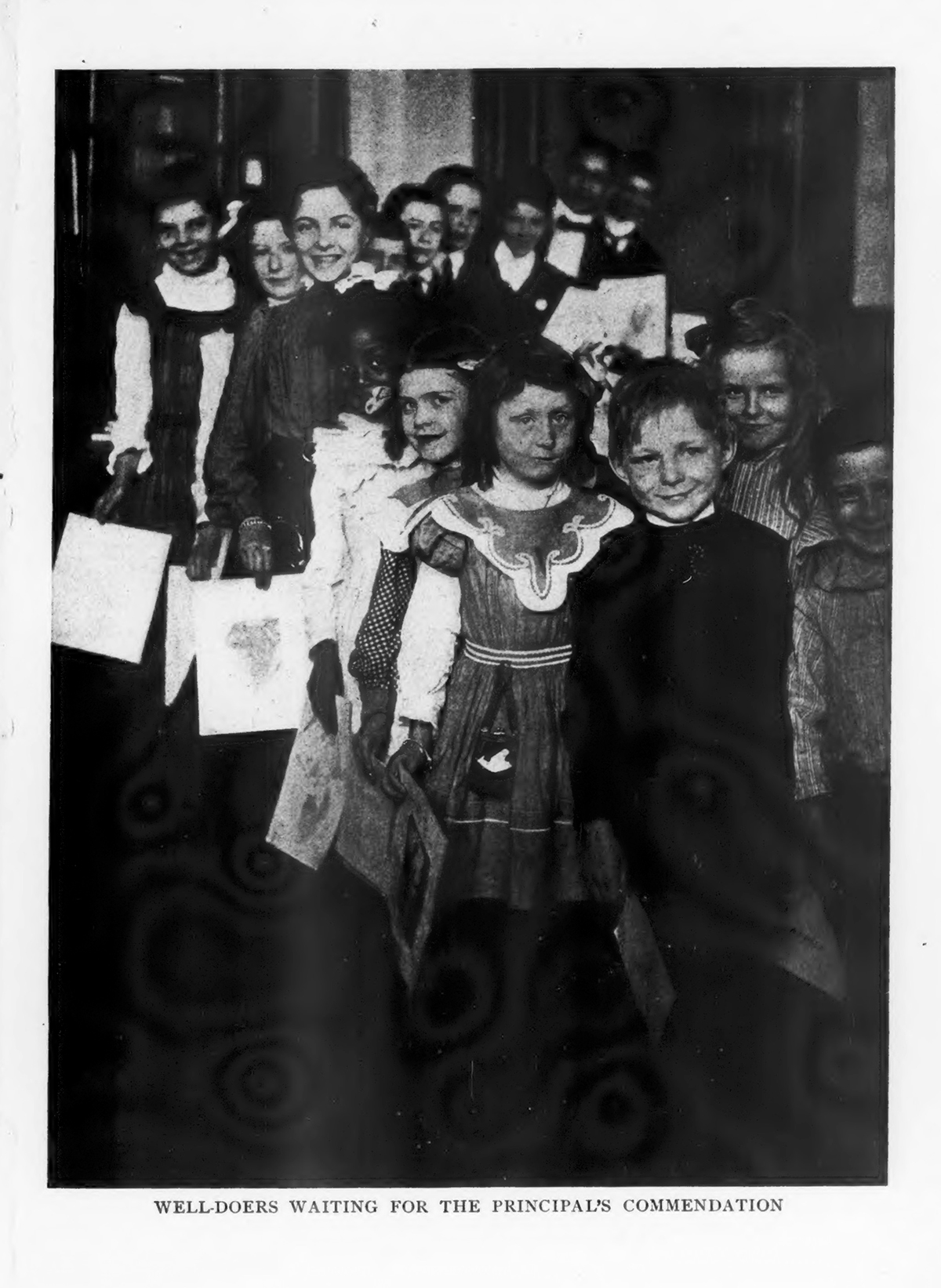 Schoolchildren of different ages are lined up, holding documents in their hands. Original caption reads &quot;Well-Doers Waiting for the Principal's Commendation&quot;