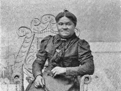 Mrs. Elizabeth Cisco is a Black woman seated in an ornate chair and wearing a formal full-length dress