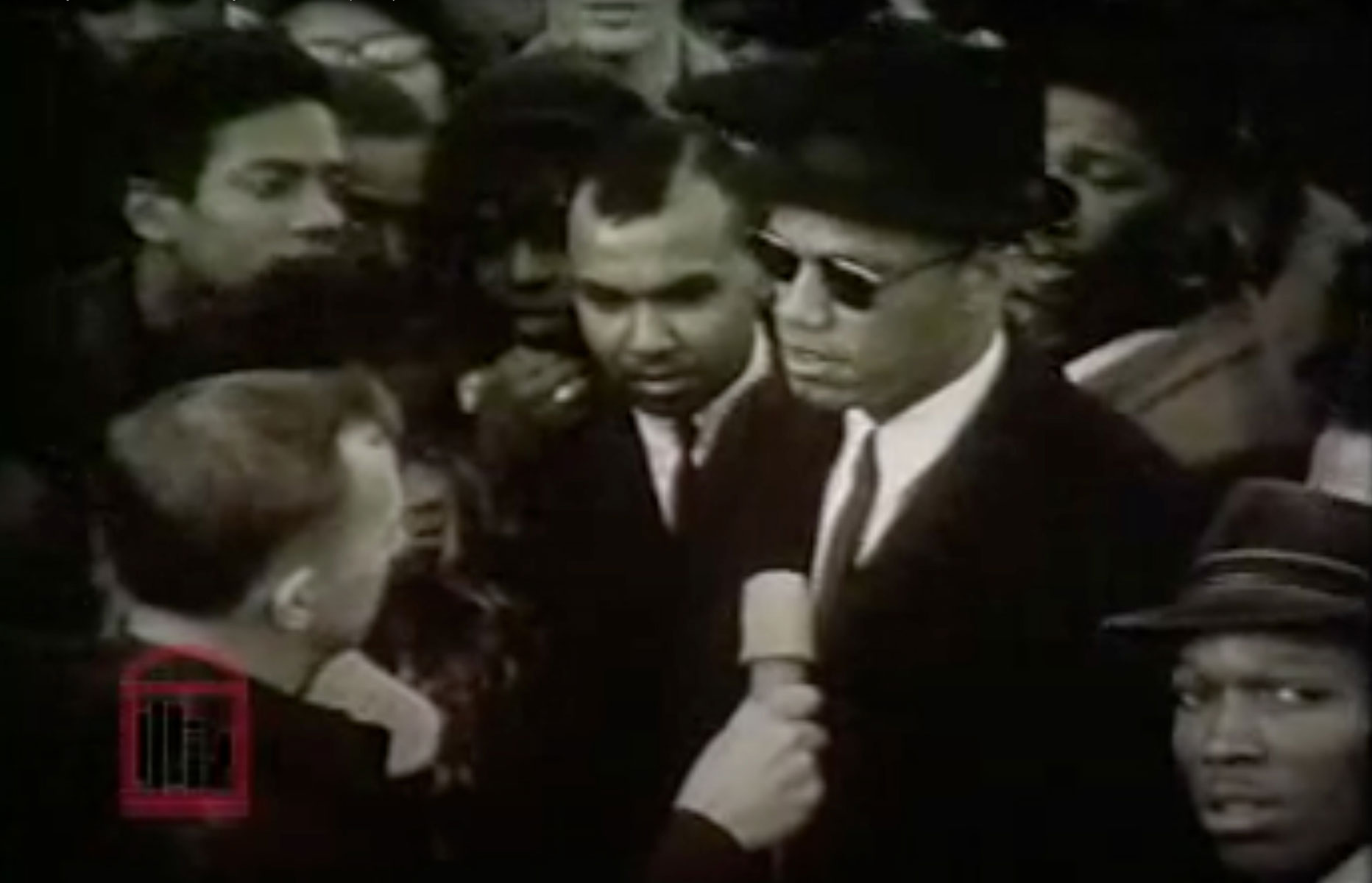 Malcolm X is interviewed while standing in front of a crowd of people.