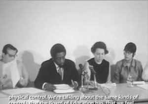 A panel of Black and Latinx parent advocates sit in front of microphones in a TV studio. Some parents read written remarks and some listen.