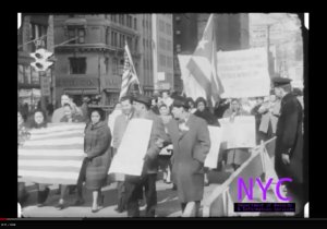 Protestors march, carrying signs and the Puerto Rican flag