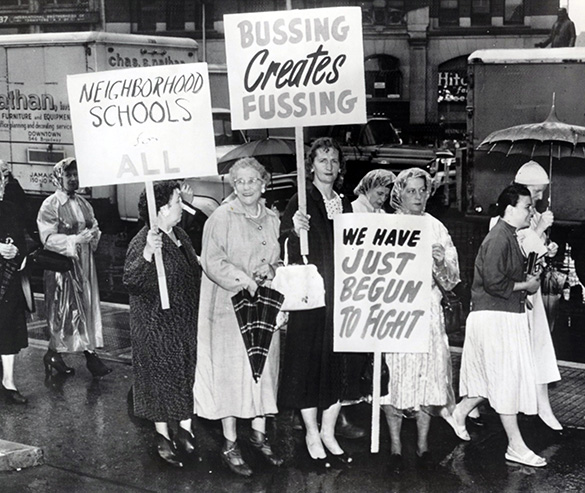 A group of white women walk in the rain and hold signs protesting desegregation.