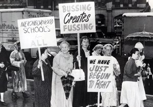 A group of white women walk in the rain and hold signs protesting desegregation.